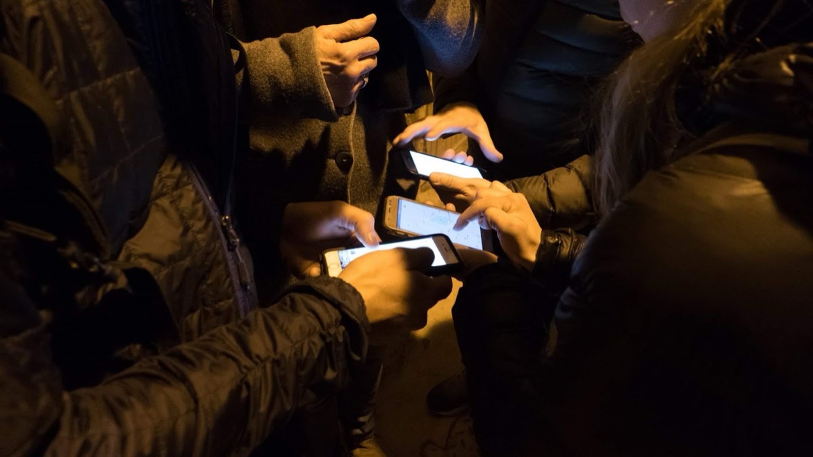 Skupina lidí večer venku nad mobilními telefony